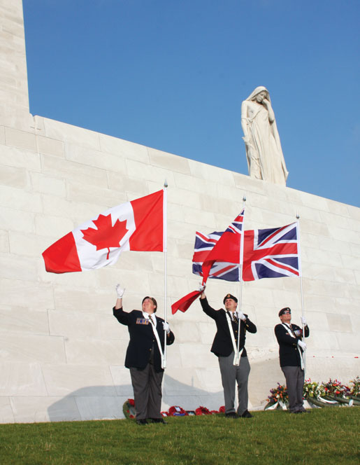 La figure endeuillée de la Mère Canada se dresse au-dessus de Belinda Wilson, de Tom MacDonald et de Tom Irvine qui récupèrent leur drapeau au monument de Vimy. [Photo : Sharon Adams]