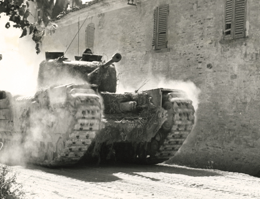 A tank kicks up dust as it moves through an Italian town during the assault on the Gothic Line. [PHOTO: LIBRARY AND ARCHIVES CANADA—PA185004]