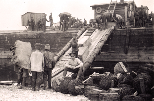 A Canadian gunner (seated) supervises prisoners as they load a barge at Yemetskoe, Northern Russia, in May 1919. [PHOTO: ALAN A. OUTRAM, LIBRARY AND ARCHIVES CANADA—PA037404]