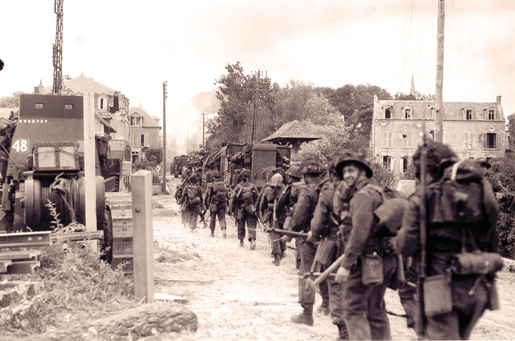Canadian soldiers and vehicles move through a village near the Normandy coast, June 6, 1944. [PHOTO: LT. FRANK L. DUBERVILL, LIBRARY AND ARCHIVES CANADA–PA131436]