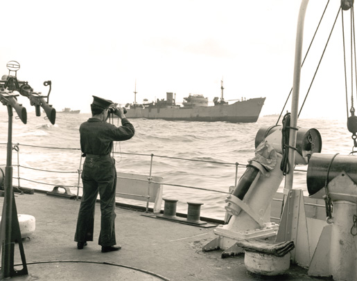 A sailor in HMCS Skeena studies the waters around an unidentified Liberty ship in 1943. [PHOTO: GERALD THOMAS RICHARDSON, LIBRARY AND ARCHIVES CANADA—PA166889]