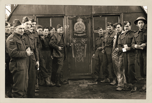 Soldiers stand next to a Canadian Legion War Services sign encouraging soldiers to write home. [PHOTO: A. LOUIS JARCHE]