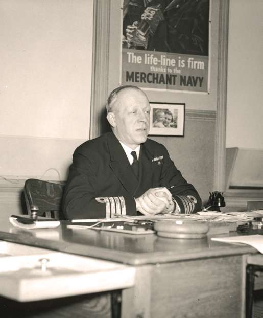 Capt. Eric S. Brand in front of a poster extolling the value of the merchant navy. [PHOTO: LIBRARY AND ARCHIVES CANADA—PA204258]