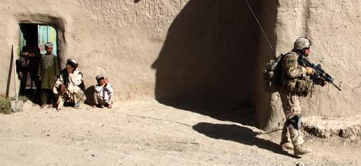 Pte. Brian Makela patrols past some villagers. [PHOTO: ADAM DAY]