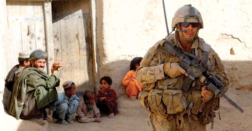 Pte. Brian Makela patrols past some villagers. [PHOTO: ADAM DAY]