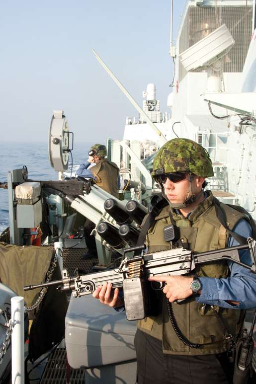 A sailor armed with a machine-gun and  wearing protective gear stands guard on Fredericton’s starboard bridge wing. [PHOTO: DAN BLACK]