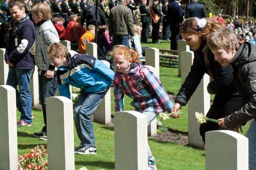 Children place flowers on the graves at Holten Canadian War Cemetery. [PHOTO: TOM MacGREGOR]