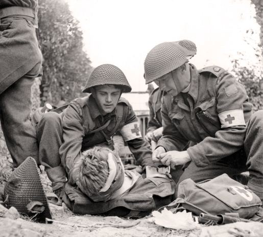 A wounded soldier is treated on the battlefield near Caen, July 15, 1944. [PHOTO: GORDON H. AIKMAN, LIBRARY AND ARCHIVES CANADA—PA133244]