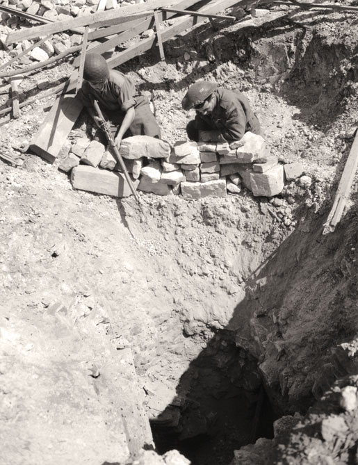 Members of Les Fusiliers Mont-Royal peer into a mine shaft used by German troops for infiltration purposes, August 1944. [PHOTO: KEN BELL, LIBRARY AND ARCHIVES CANADA—PA131353]