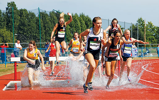 Athletes run through the water in the youth girls 2,000-metre steeplechase. [PHOTO: ADAM DAY]