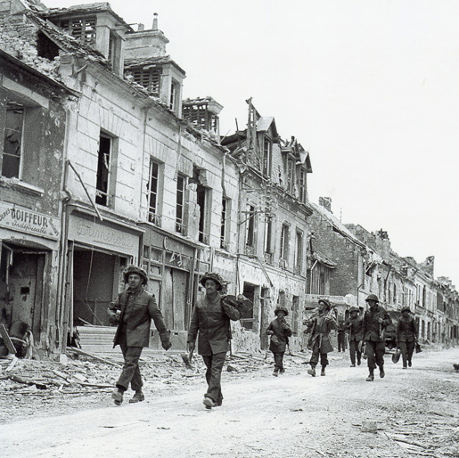 Canadian infantry walking through rubble. [PHOTO: LIBRARY AND ARCHIVES CANADA—PA162651]