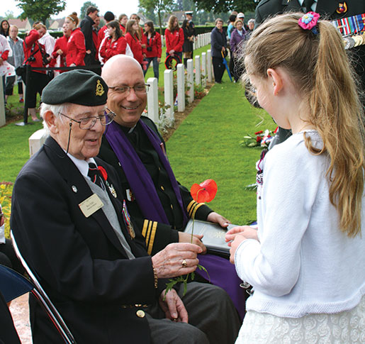 Roy Eddy receives a poppy from a young girl at Bretteville-sur-Laize Canadian War Cemetery. [PHOTO: SHARON ADAMS]