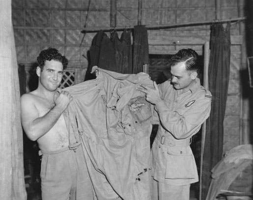 Squadron Leader James Bell (left) and Flying Officer Malcolm Forester display a flying suit that was ripped and torn by Japanese shell splinters. [PHOTO: LIBRARY AND ARCHIVES CANADA—PL-27691]
