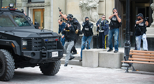 Chief of Defence Staff  General Tom Lawson  is hustled away from Parliament Hill on  Oct. 22, 2014, as security forces scan nearby rooftops for shooters. [Ashley Fraser/Ottawa Citizen. Reprinted by permission.]
