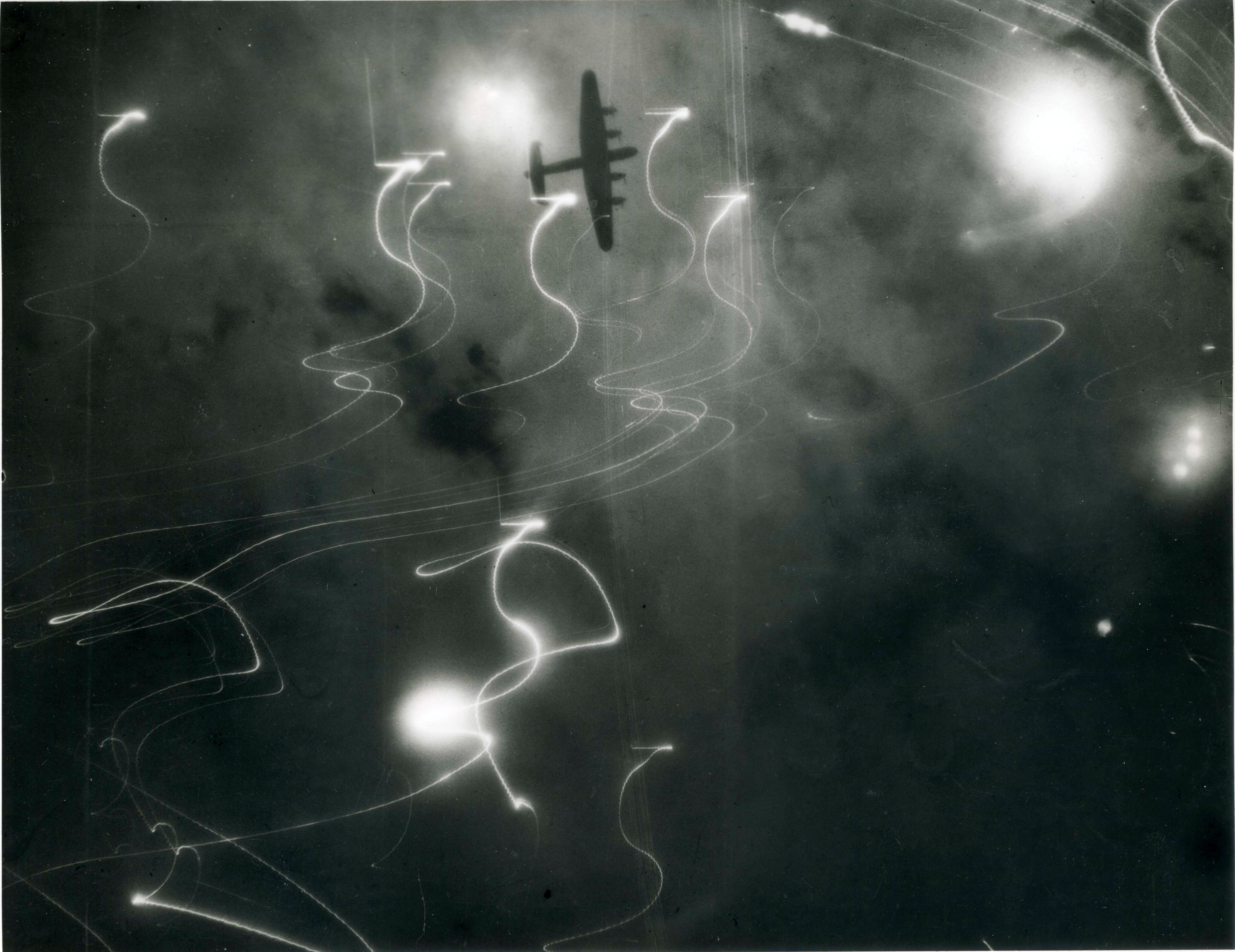 An Avro Lancaster of No 1 Group, Bomber Command, silhouetted against flares, smoke and explosions during the attack on Hamburg, Germany, by aircraft of Nos 1, 5 and 8 Groups on the night of 30/31 January 1943. This raid was the first occasion on which H2S centimetric radar was used by the Pathfinder aircraft to navigate the force to the target. Credit: Imperial War Museum