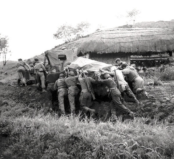 Soldiers push a jeep and trailer up a muddy slope