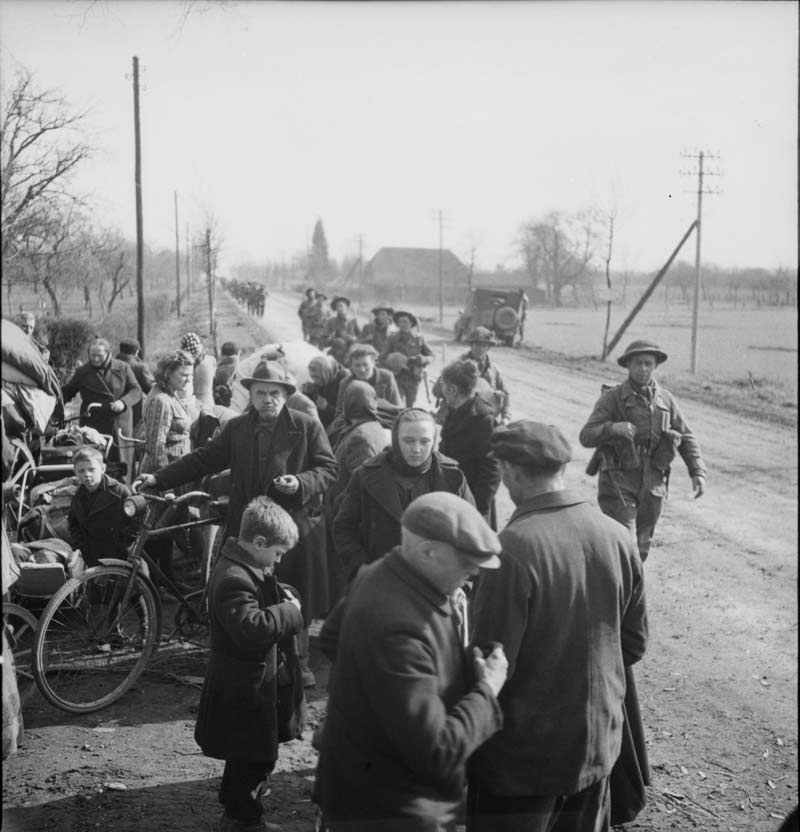 Refugees with their belongings, while members of the 2 Canadian Infantry Division file past. Xanten, Germany, 9 Mar. 1945