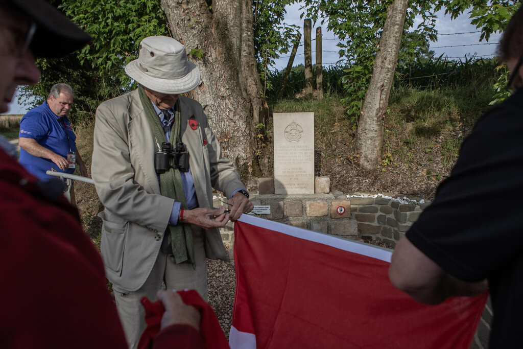 People hold a Canadian flag in front of a monument in France